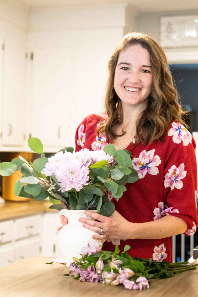 Woman standing in her kitchen with a white pitcher of flowers