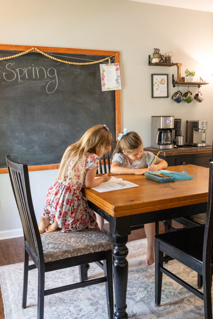 two girls sitting at a table with chalk board behind them