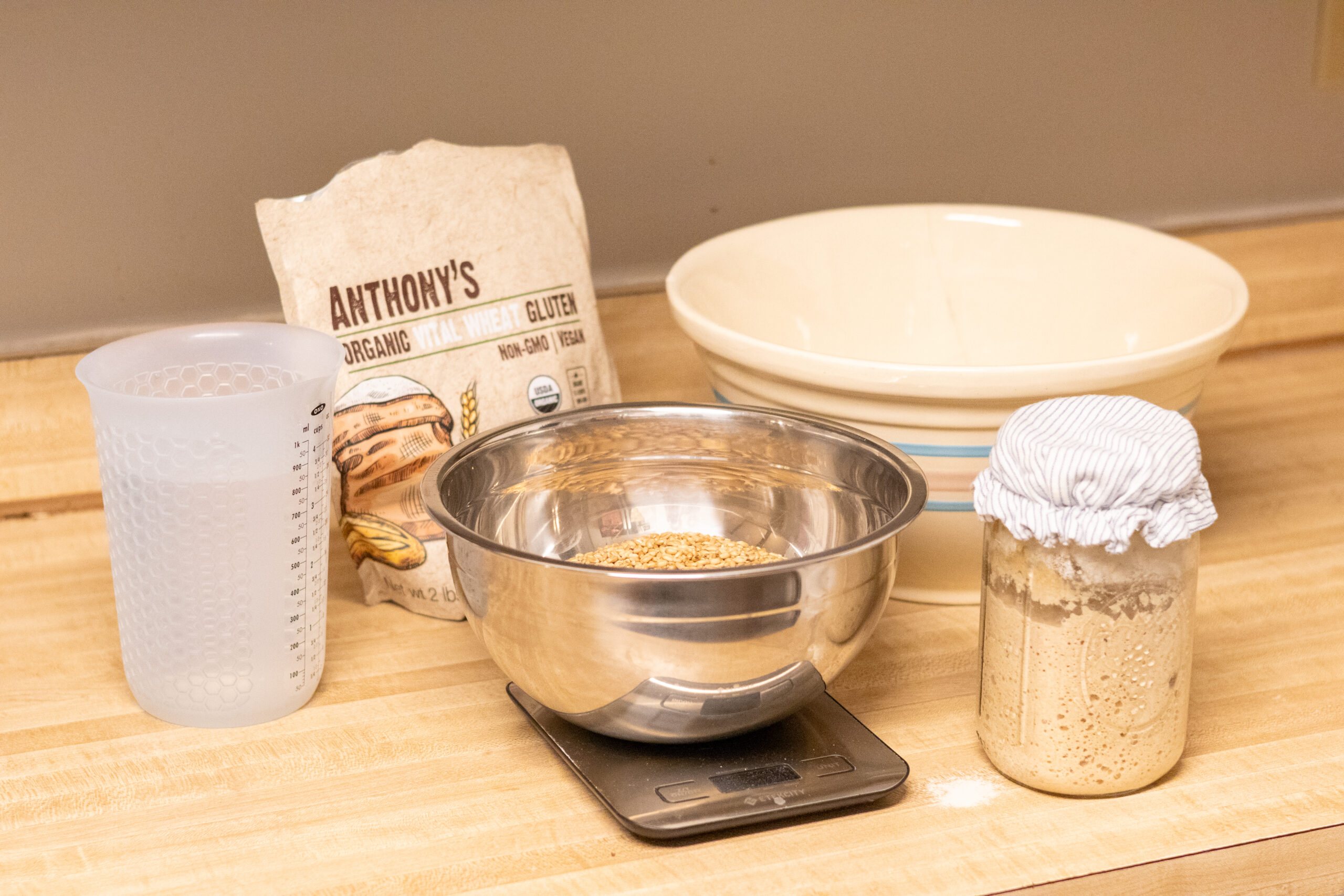 Water, flour, gluten, salt, and sourdough starter sitting on the counter with a kitchen scale. Ingredients for sourdough bread.