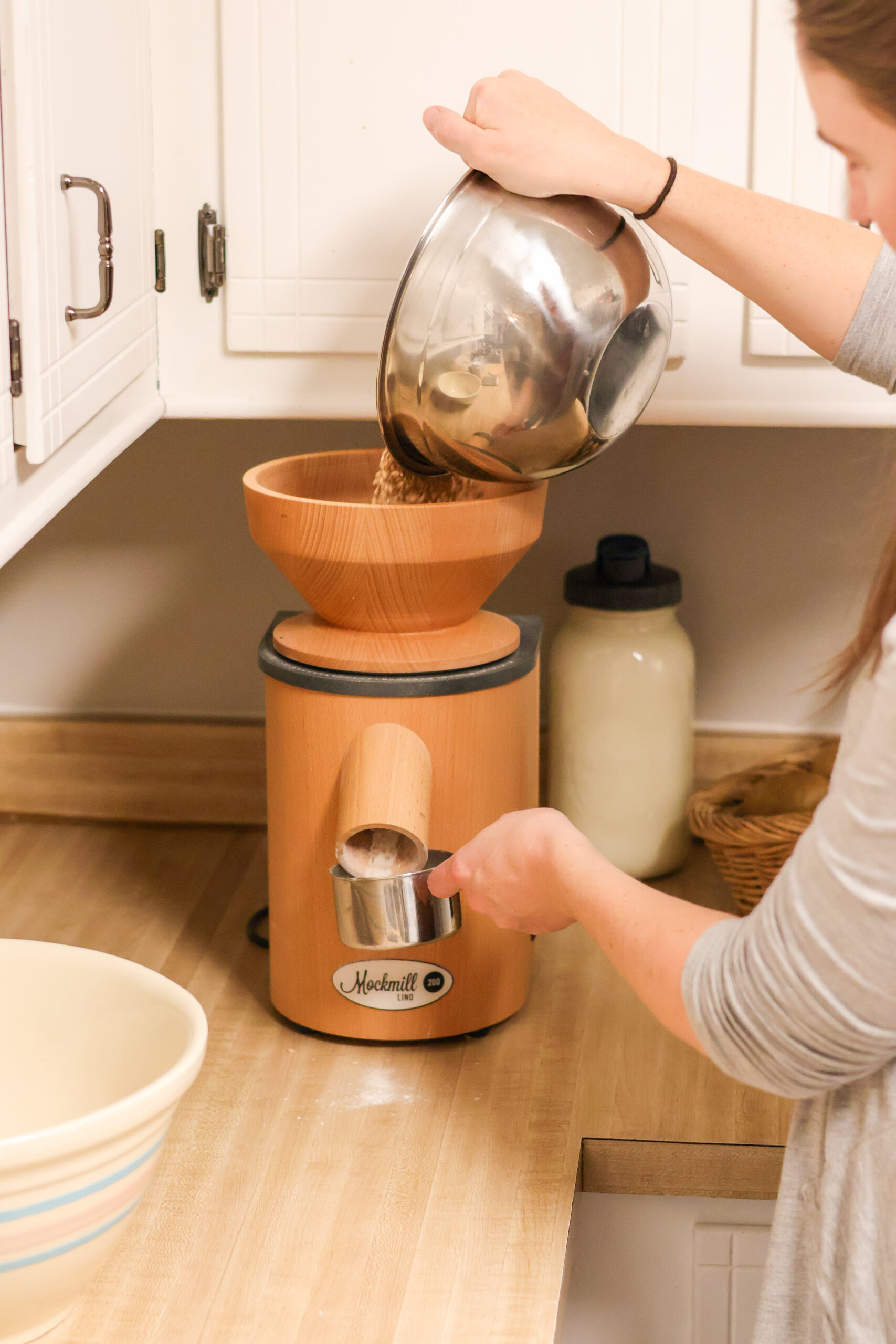 Woman pour wheat berries into an at home flour mill in her kitchen