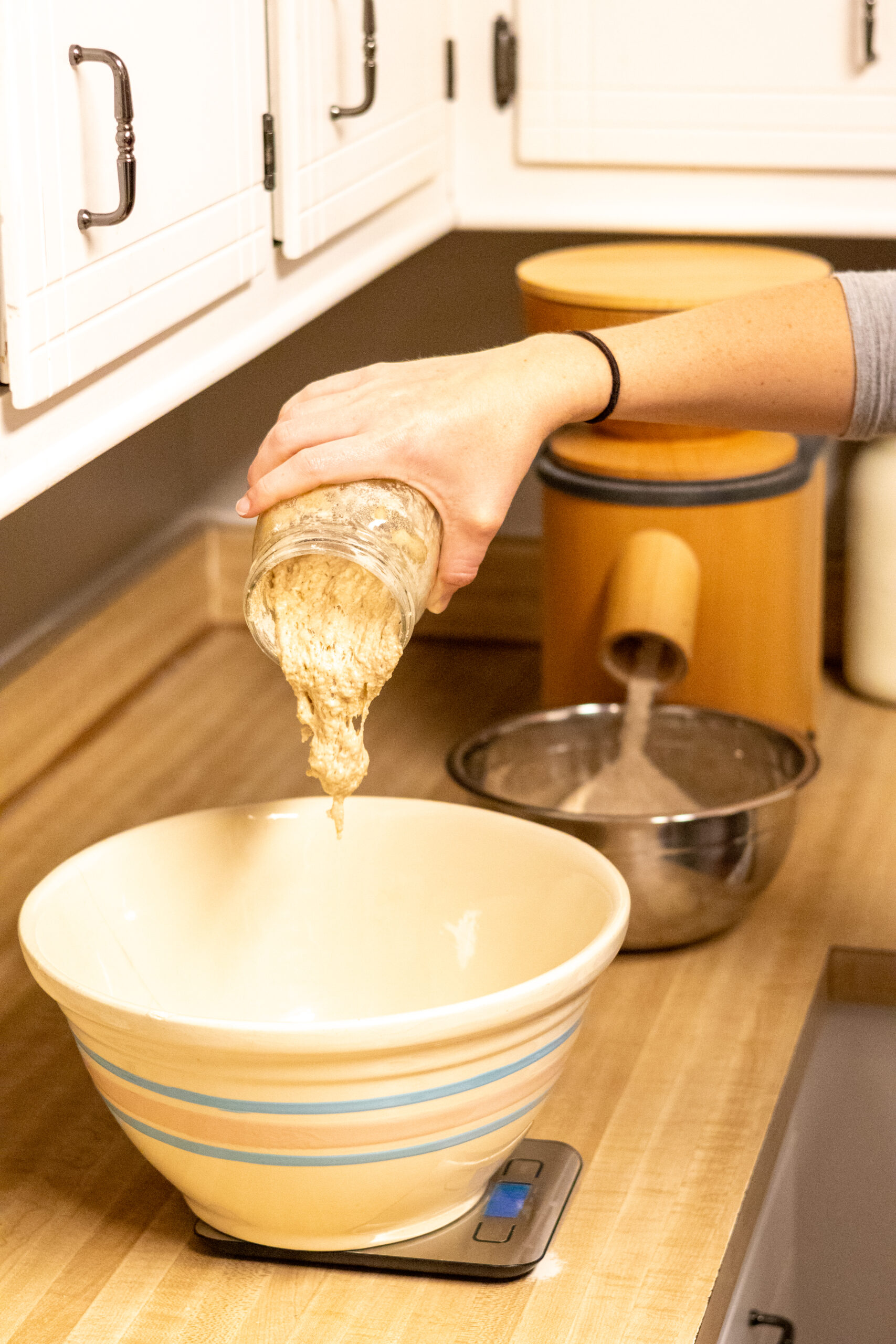 Woman measuring sourdough starter into a bowl with kitchen scale