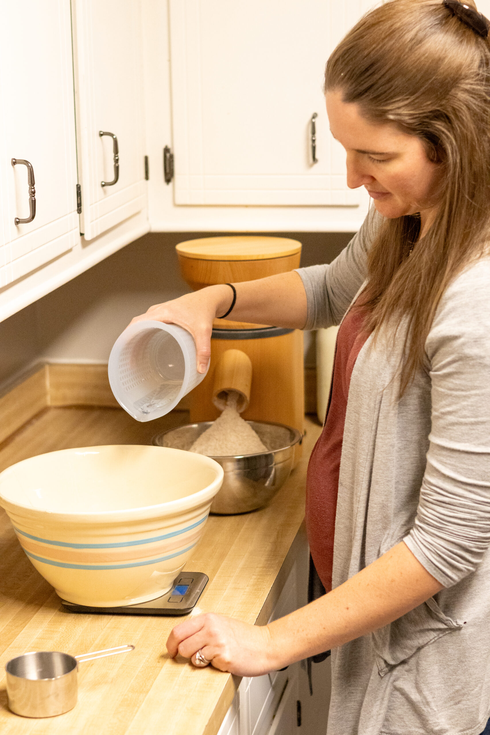 Pouring water into a bowl that is sitting on a kitchen scale