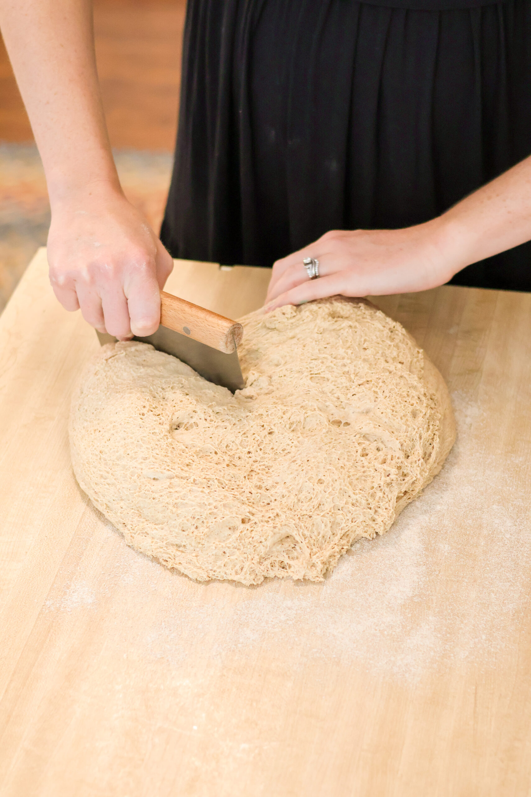 Using a bench scraper to divide soudough into two loaves