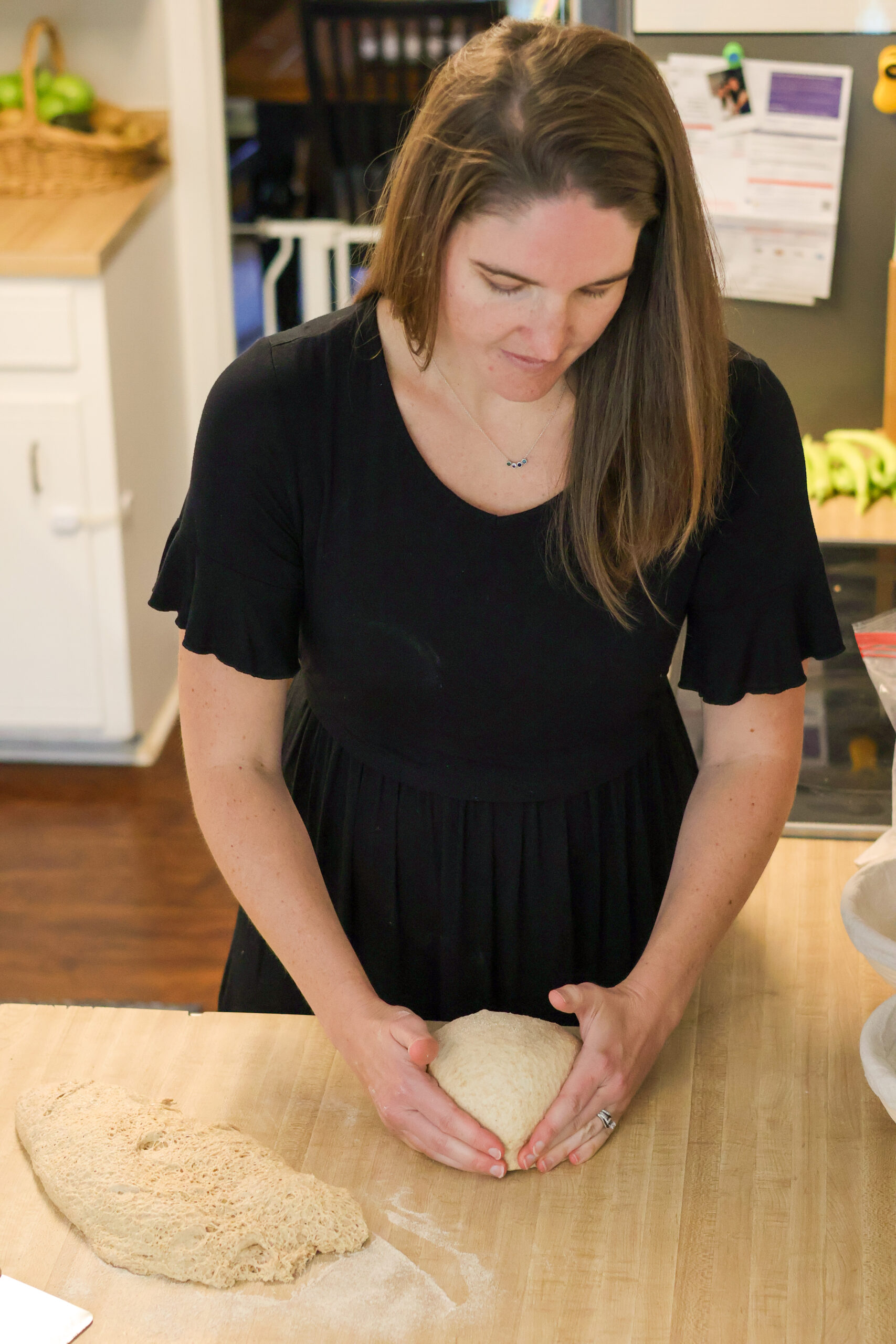 Woman shaping sourdough loaf of bread on counter top