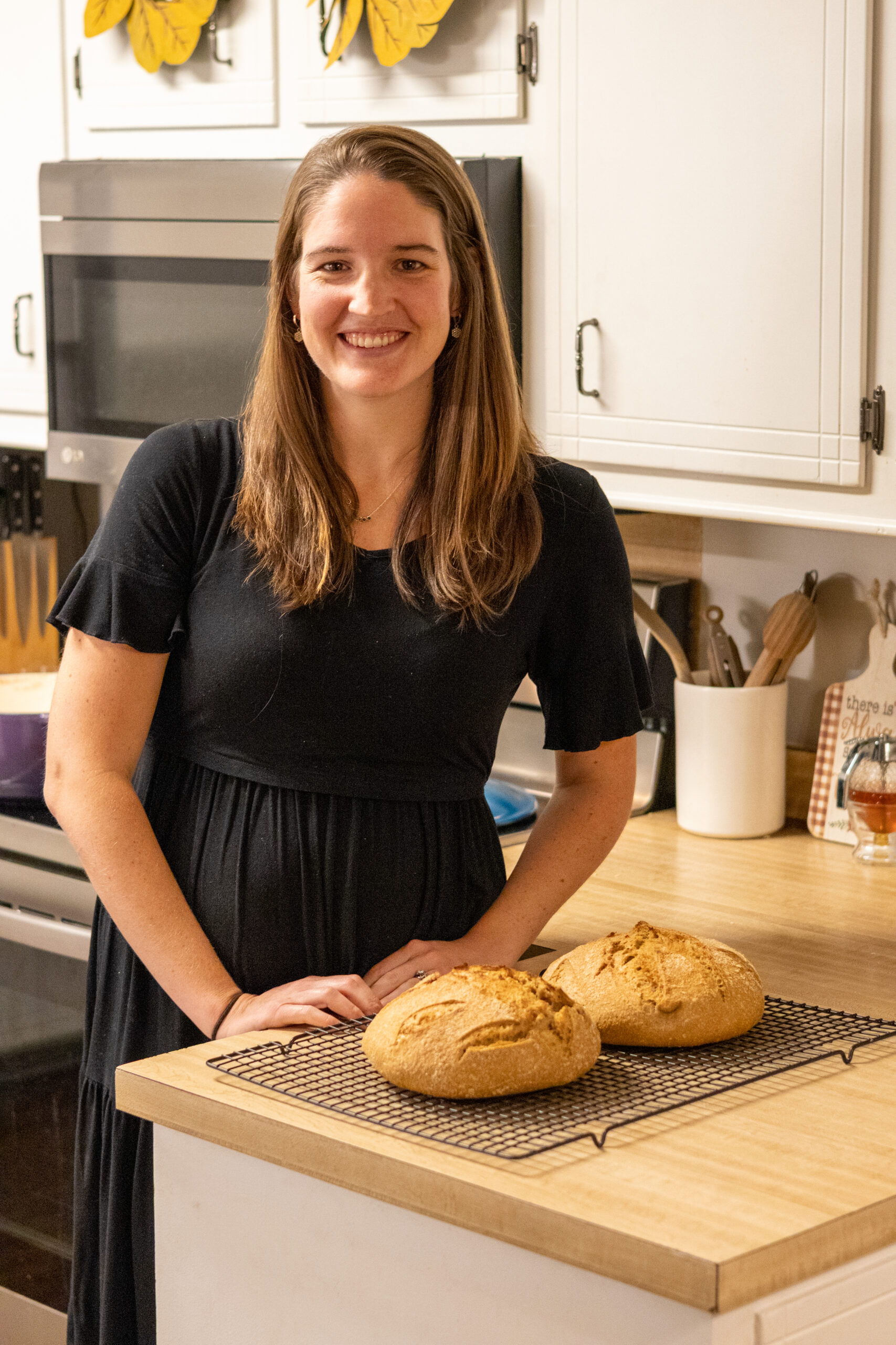 Woman standing in the kitchen with two loaves of freshly milled artisan sourdough bread on the counter top